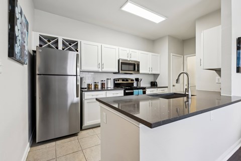 A modern kitchen with a stainless steel refrigerator and white cabinets.at Flats on Chapel, Waco, TX  